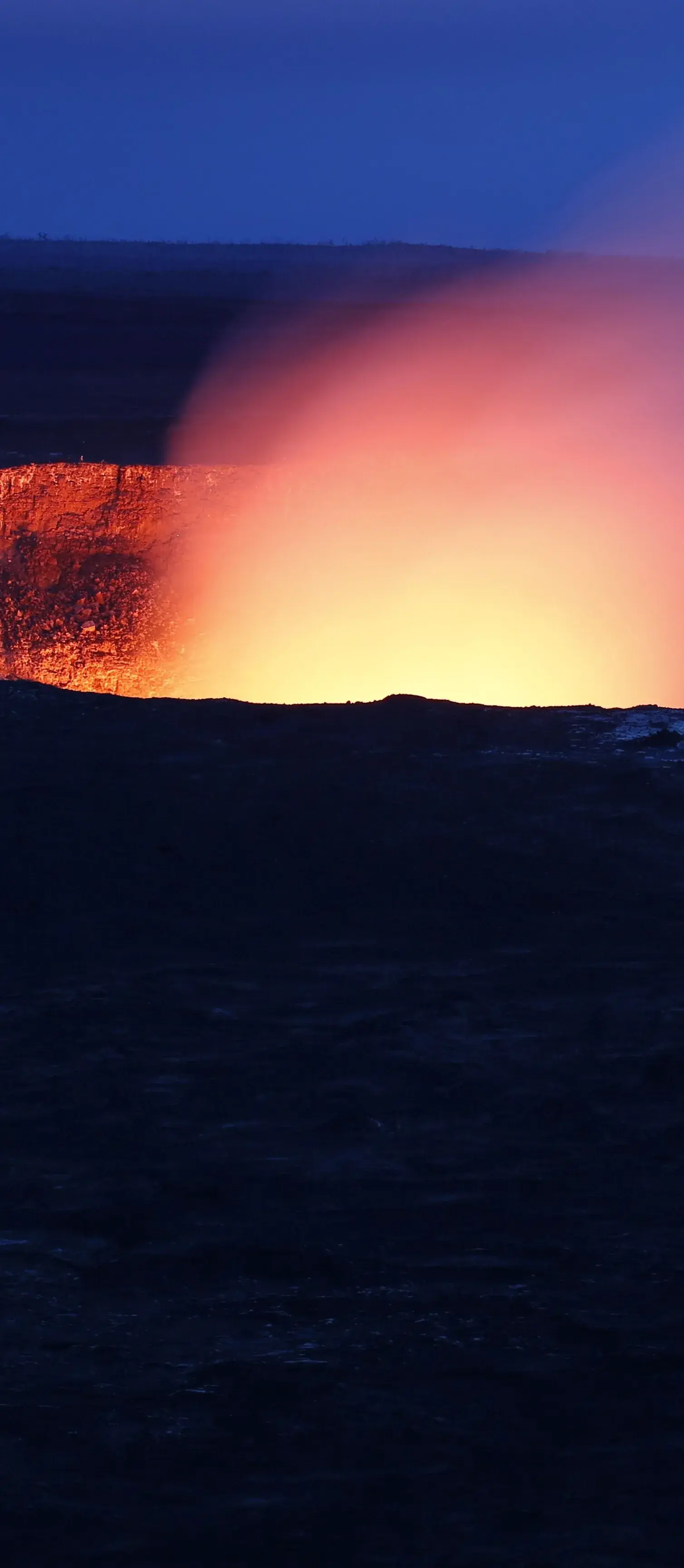 A crater glowing orange at dusk, its plume drifting across a deep blue sky